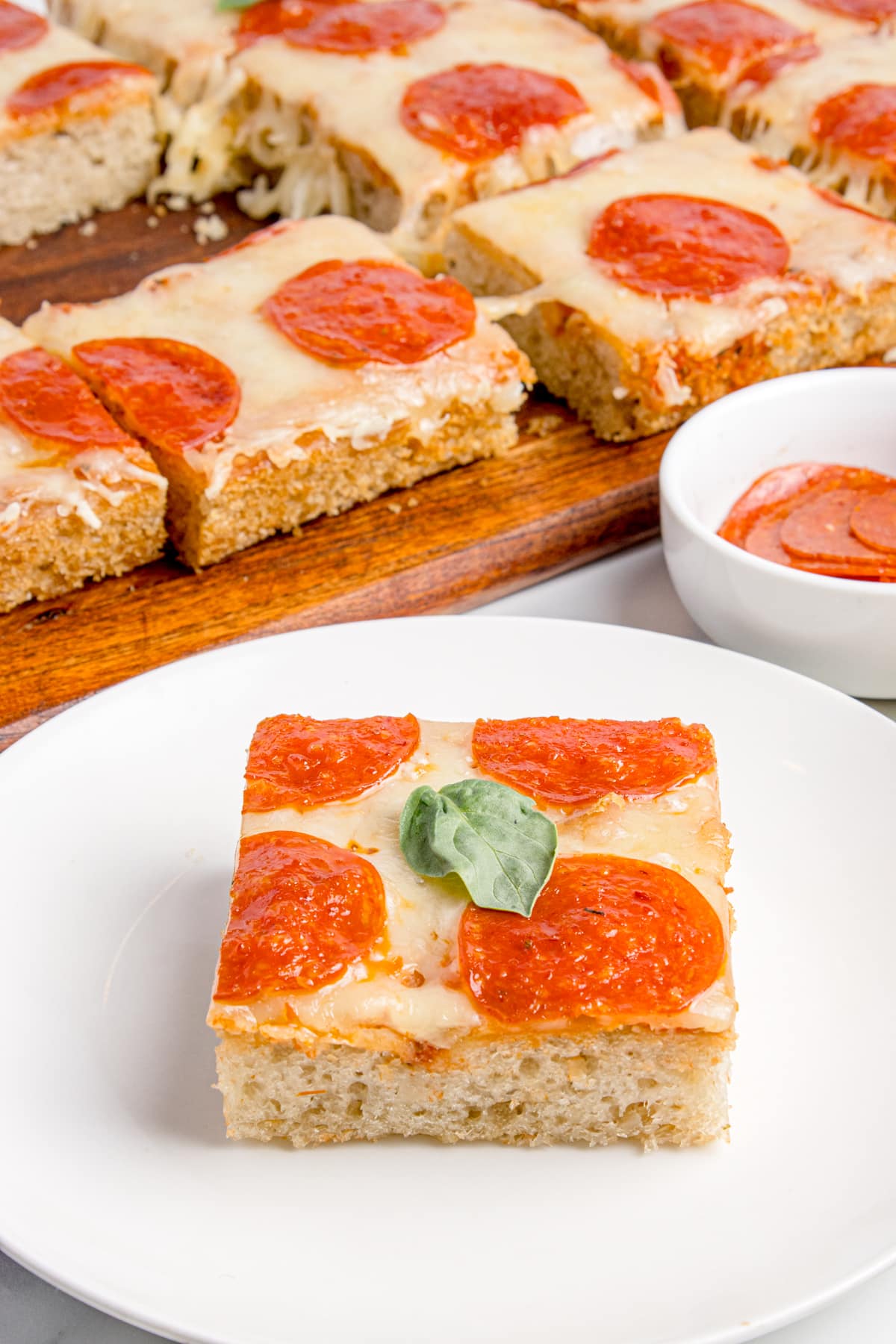 slice of focaccia pizza on white plate with rest of pizza in background on wooden cutting board