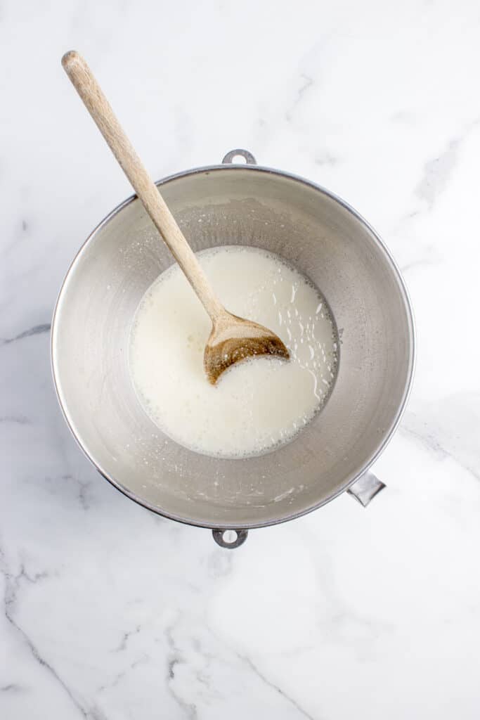 metal mixing bowl with sourdough starter and flour and wooden spoon