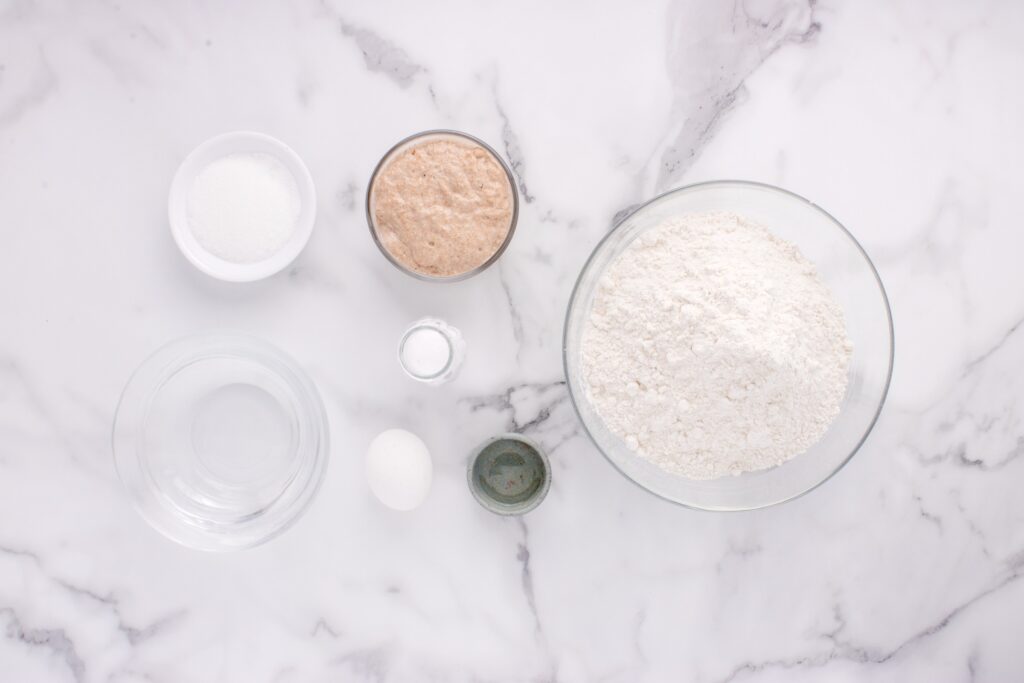 ingredients for sourdough French bread in glass bowls on marble counter
