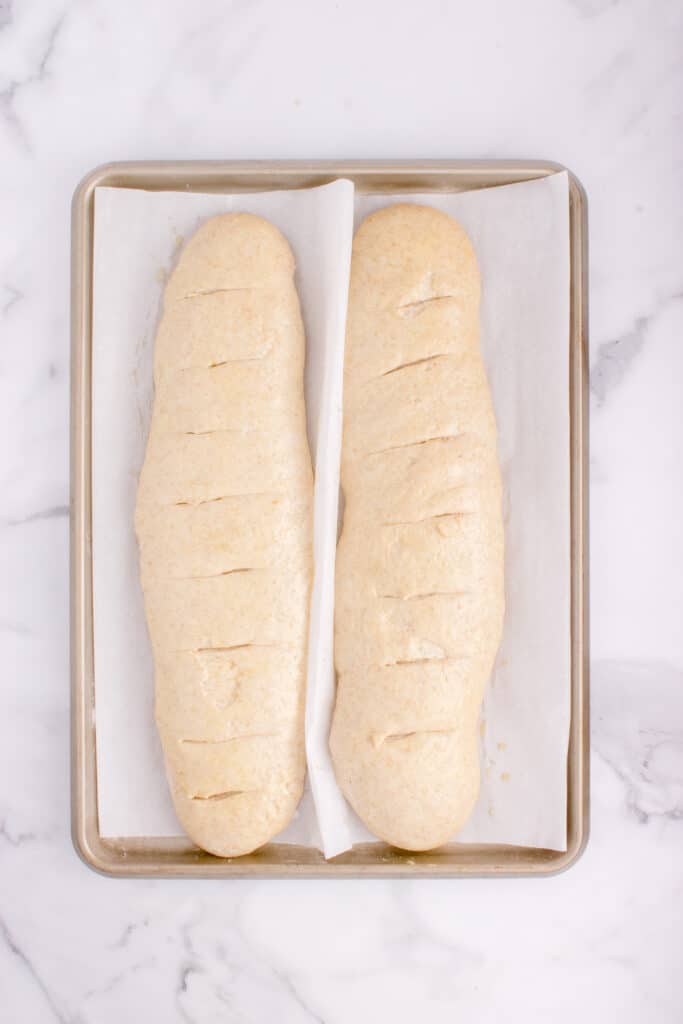 two loaves of French bread on baking tray after being sliced and ready to bake