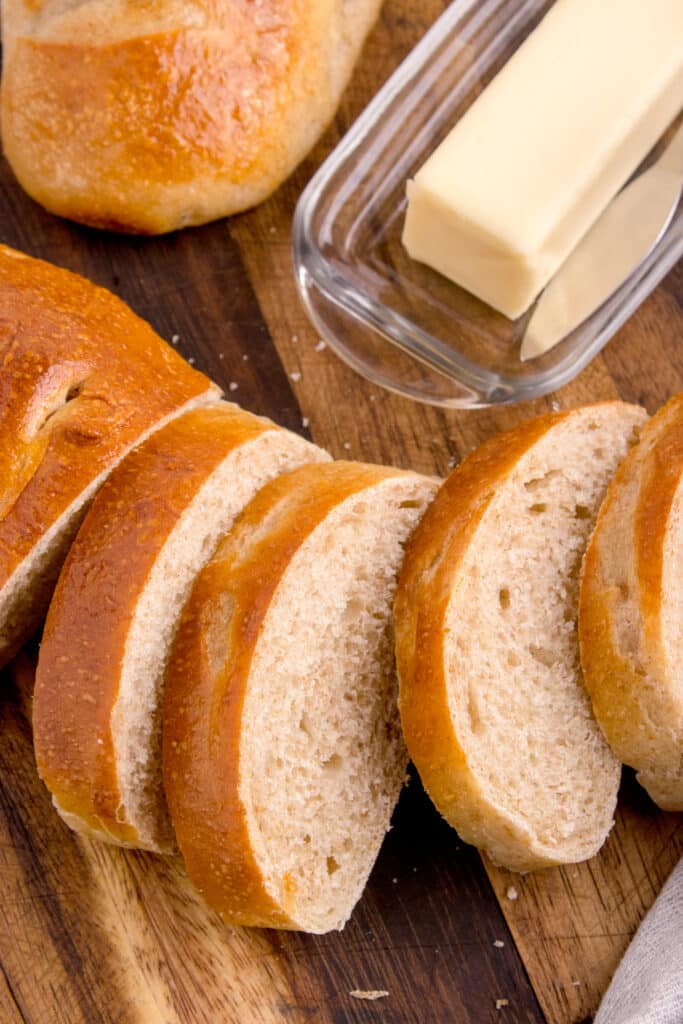 slices of sourdough French bread lined up on cutting board with butter beside