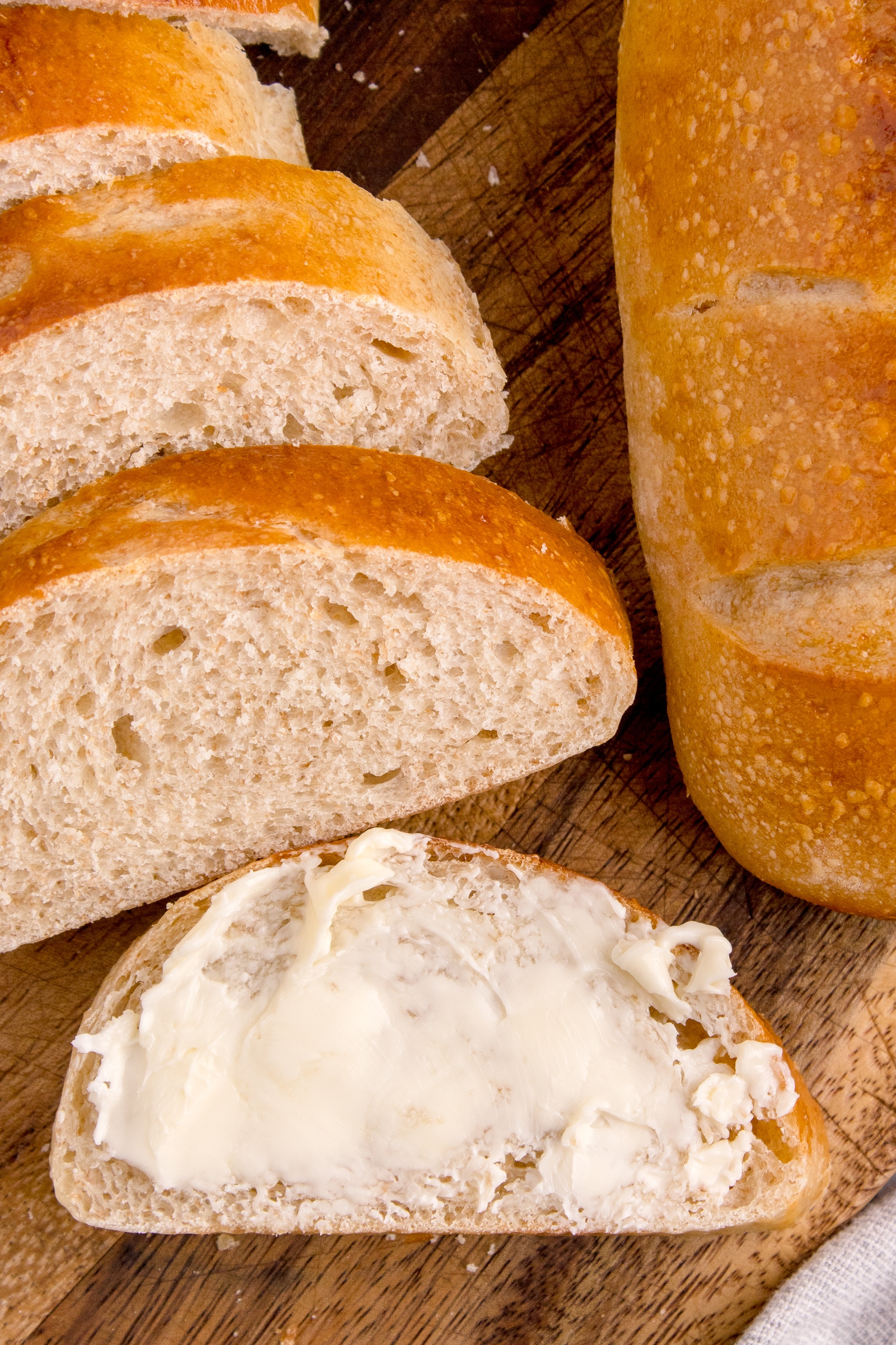 slices of sourdough French bread on cutting board stacked together with front slice spread with butter