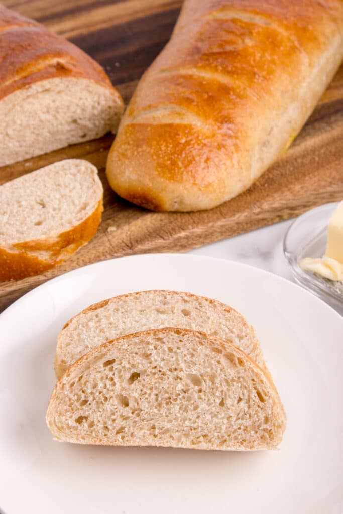 two slices of sourdough French bread on white plate with loaves in background