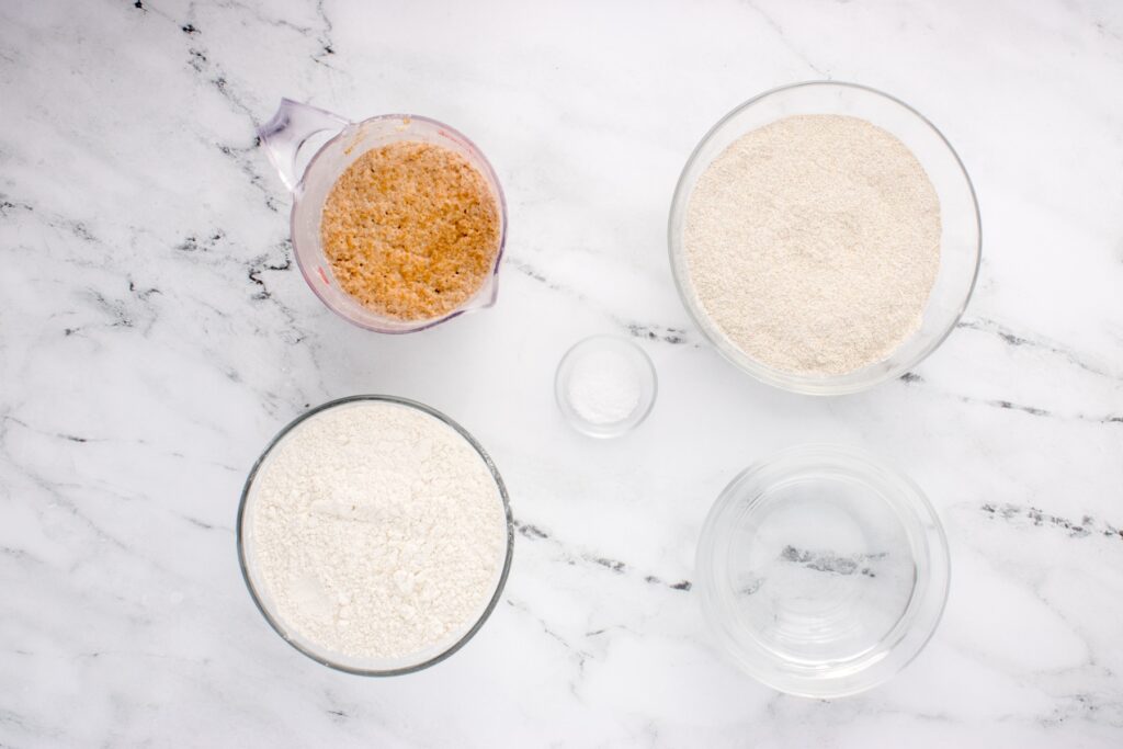 ingredients for sourdough rye bread in glass bowls on marble counter