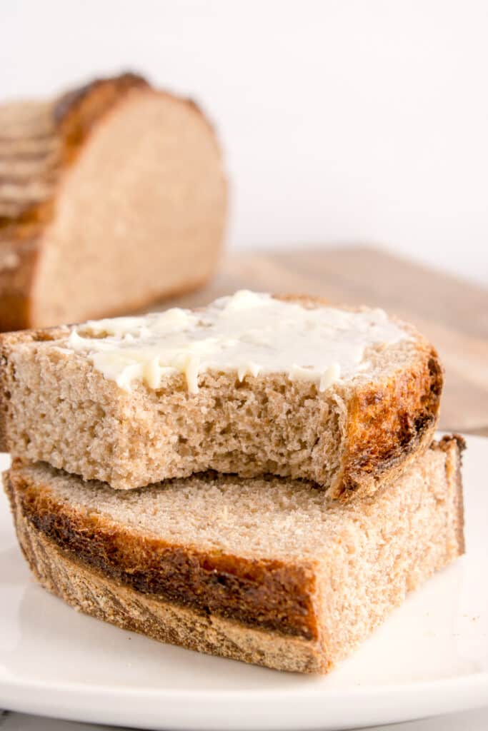 slices of sourdough rye stacked on top of each other with top slice being buttered and having a bite taken out