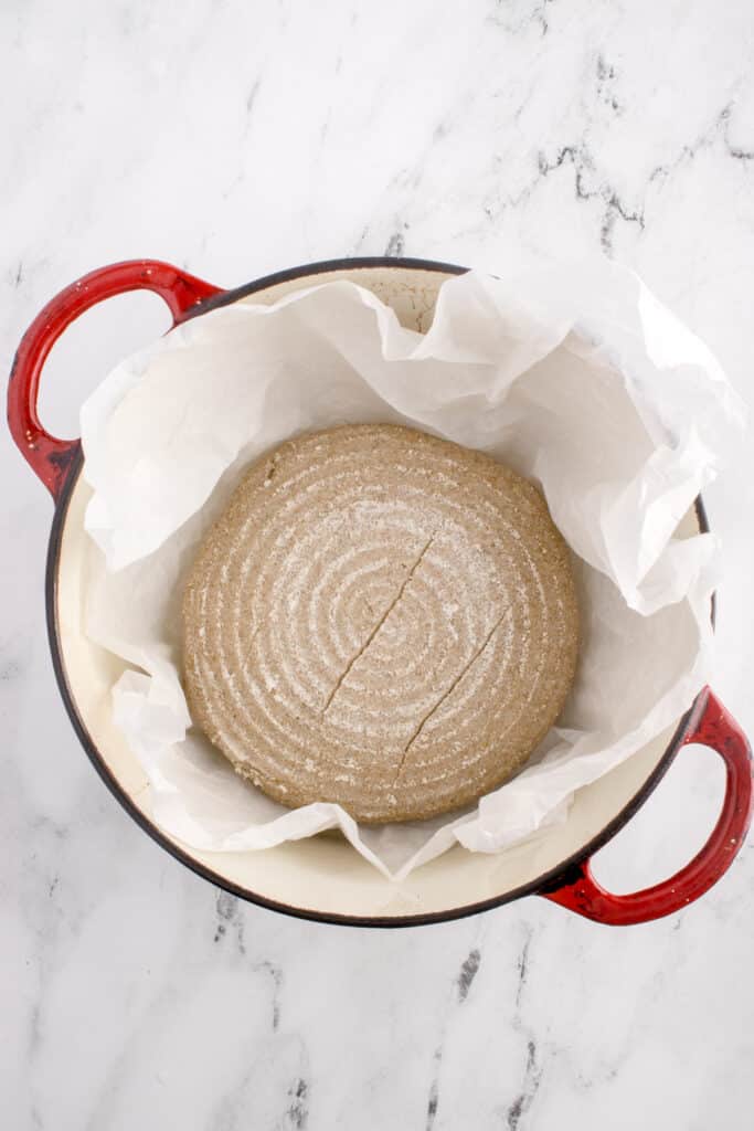 red cast iron enameled pan with parchment paper and dough for sourdough rye ready to be baked