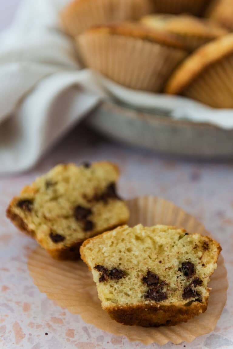 sourdough chocolate chip muffin cut open to show inside on paper liner with bowl of more muffins in background