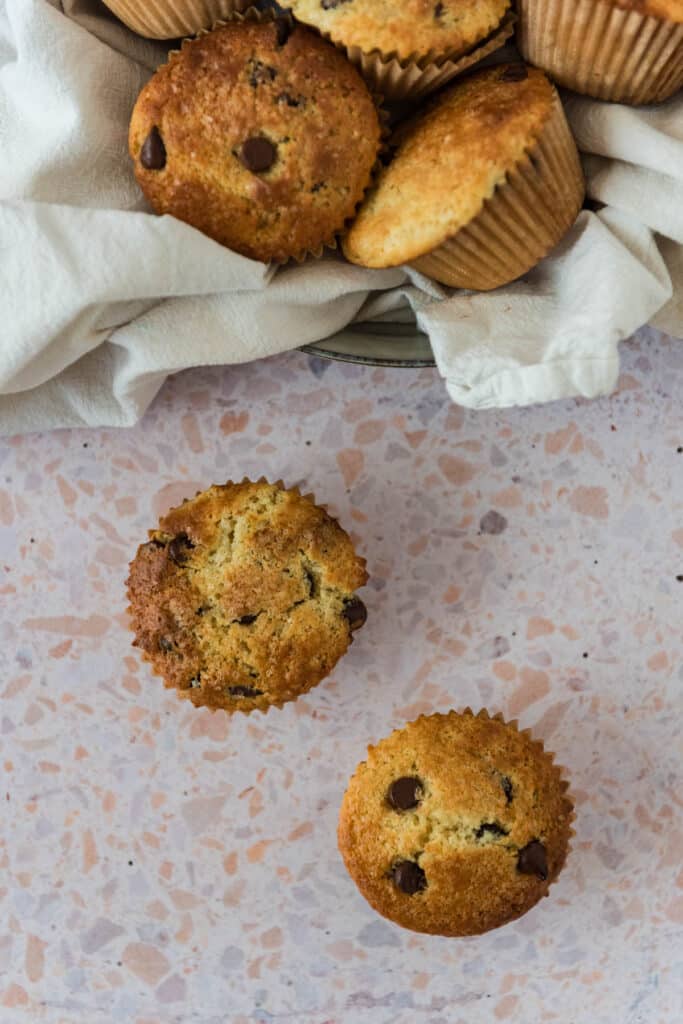 bowl with kitchen towel and sourdough chocolate chip muffins in bowl, with two on counter beside bowl