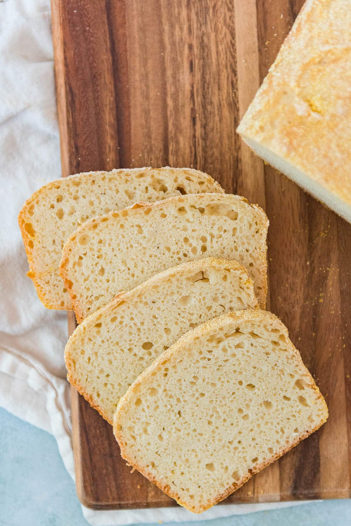 four slices of sourdough english muffin bread on wooden cutting board with loaf on the side