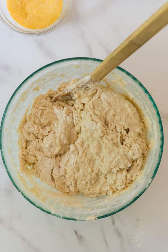 glass mixing bowl with mixed dough for sourdough English muffins and wooden spoon