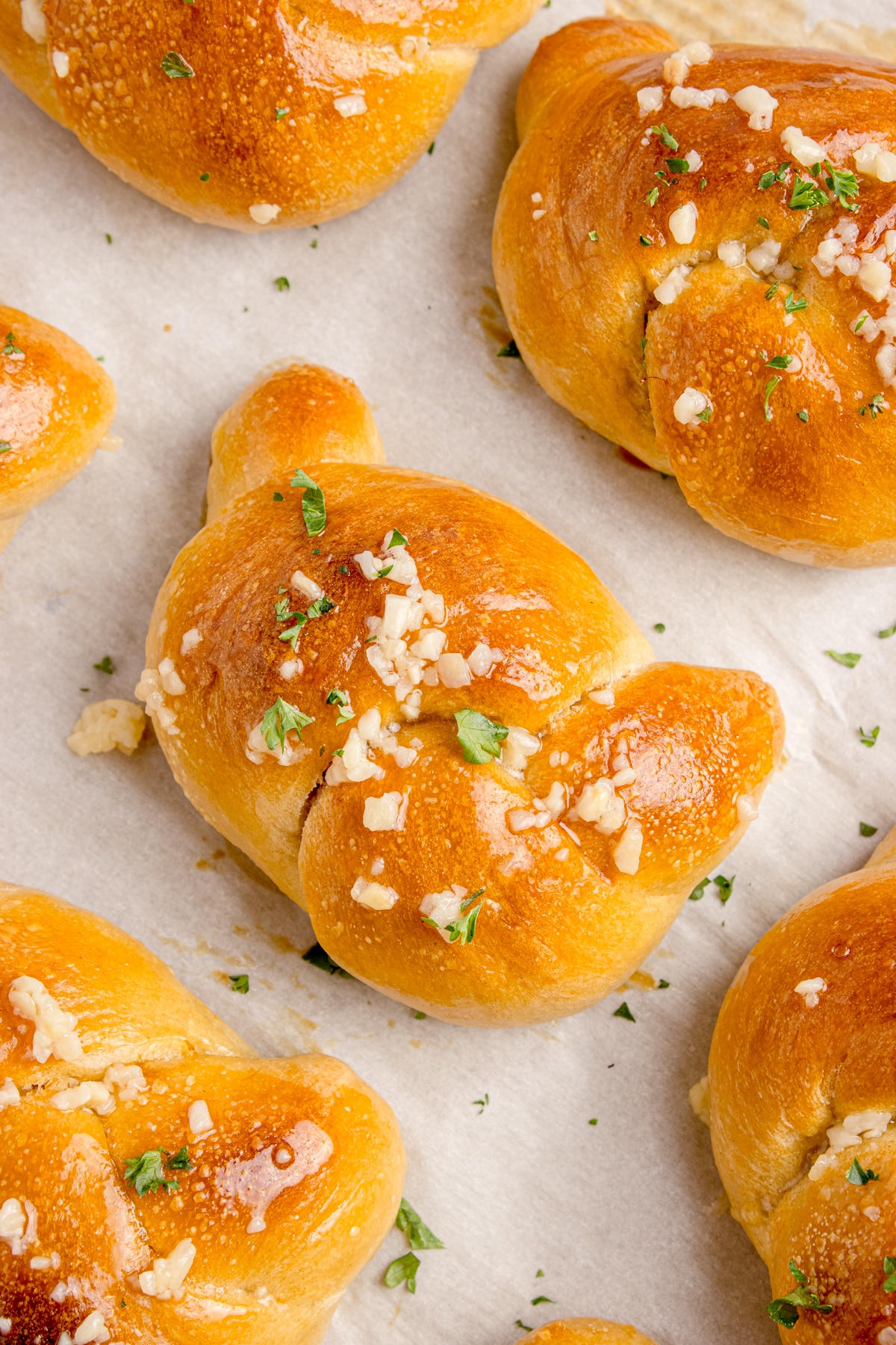 closeup of sourdough garlic knots on parchment paper with garlic butter on top