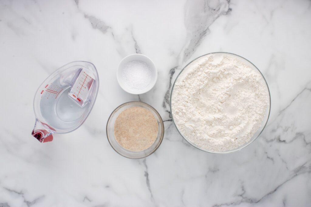 ingredients for sourdough baguette in glass bowls on marble counter