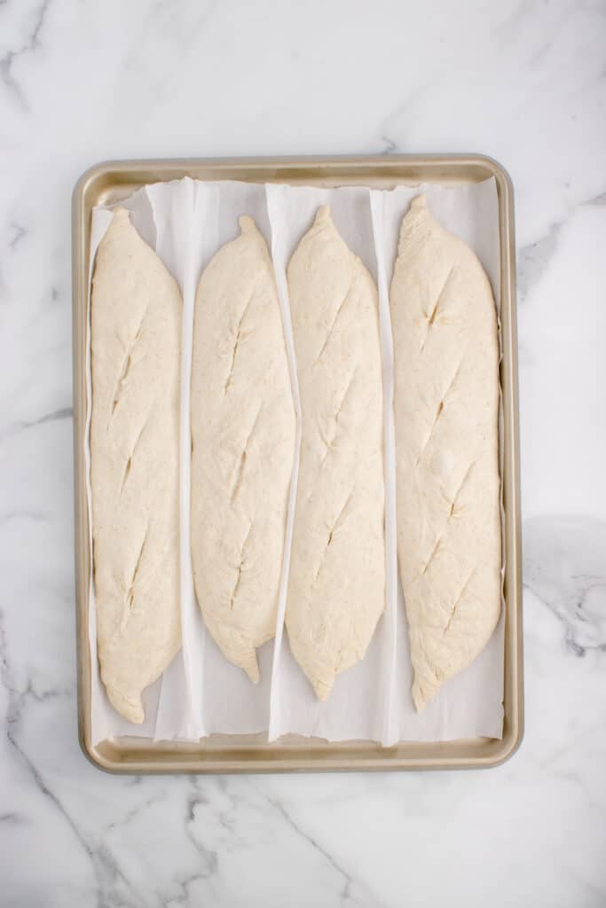 four sourdough baguette on baking pan with score marks