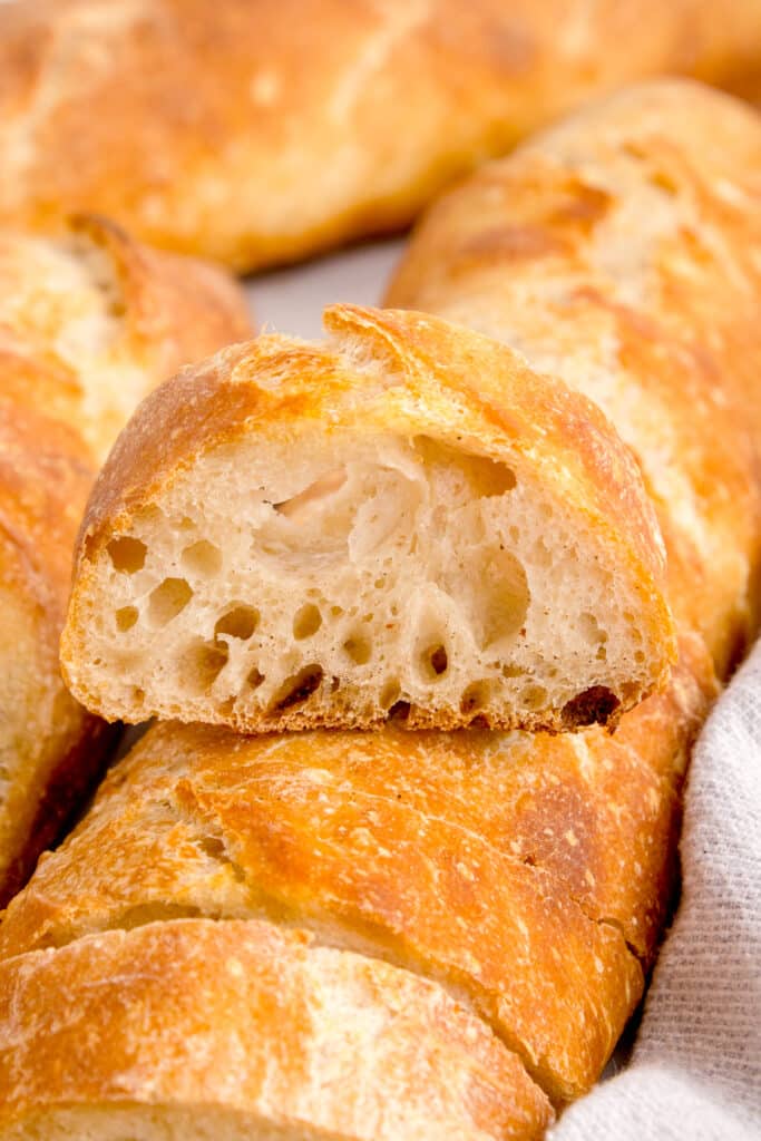 slice of sourdough baguette balanced on top of other baguette loaves