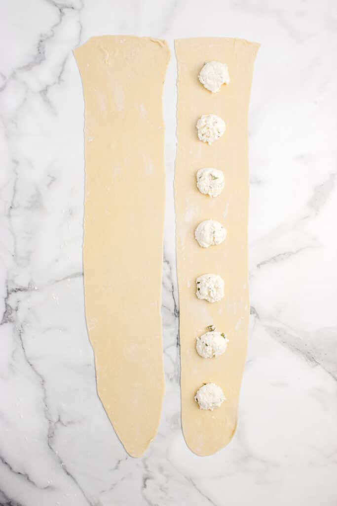 two strips of sourdough ravioli dough rolled into rectangles with small balls of cheese filling on right strip