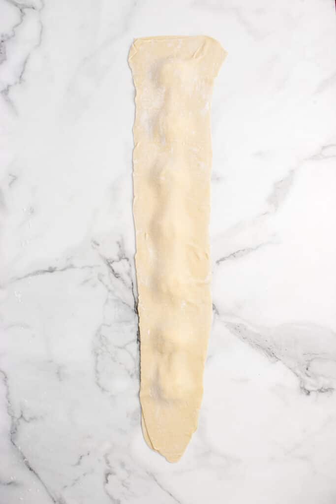 sourdough ravioli dough rolled into a strip with balls of cheese filling in the middle and second strip on top