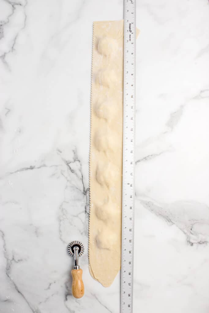 strip of assembled sourdough cheese raviolis with ruler and dough cutter