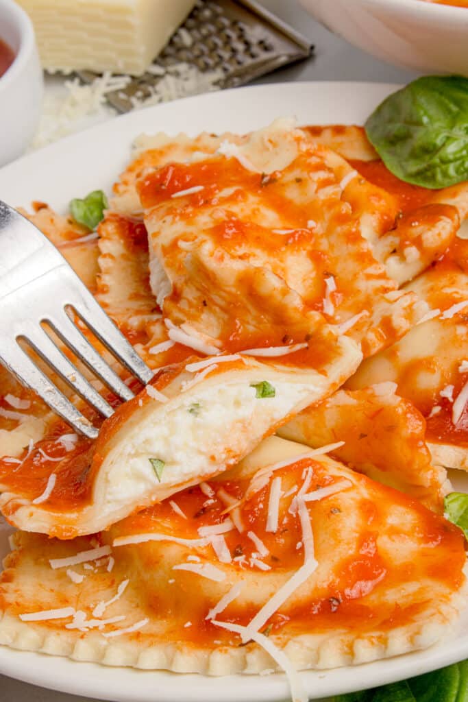 plate of sourdough cheese ravioli with sauce with one ravioli cut in half on fork to show cheese filling