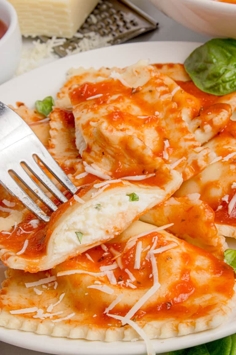 plate of sourdough cheese ravioli with sauce with one ravioli cut in half on fork to show cheese filling