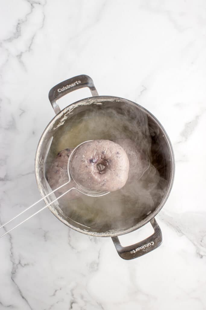 spoon pulling bagel from boiling water