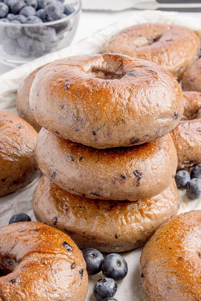 stack of three sourdough blueberry bagels with more bagels and blueberries around it