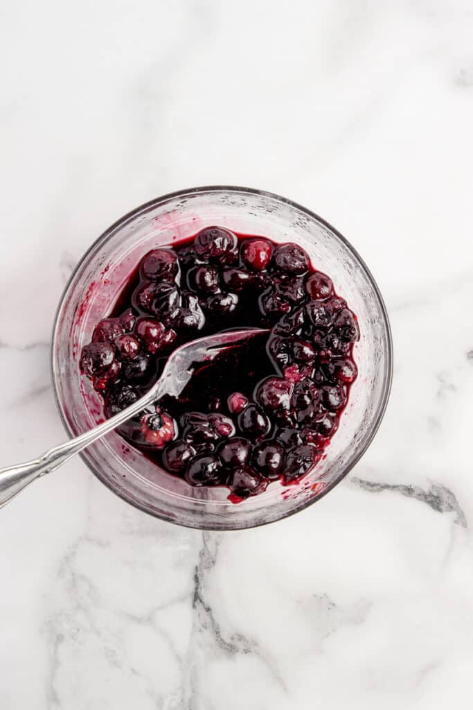 glass bowl with mashed blueberries and fork on marble counter
