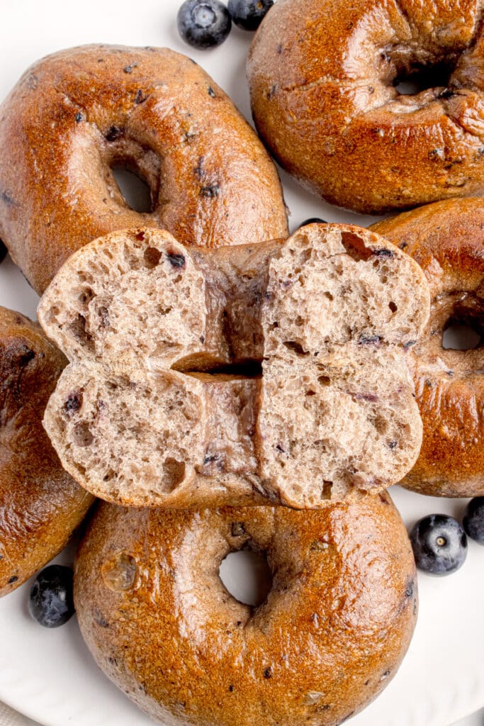 batch of sourdough blueberry bagels with one bagel split in half to show inside texture