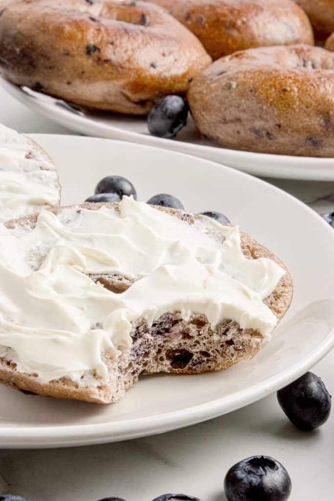 blueberry sourdough bagel sliced in half with cream cheese on top and bite taken out