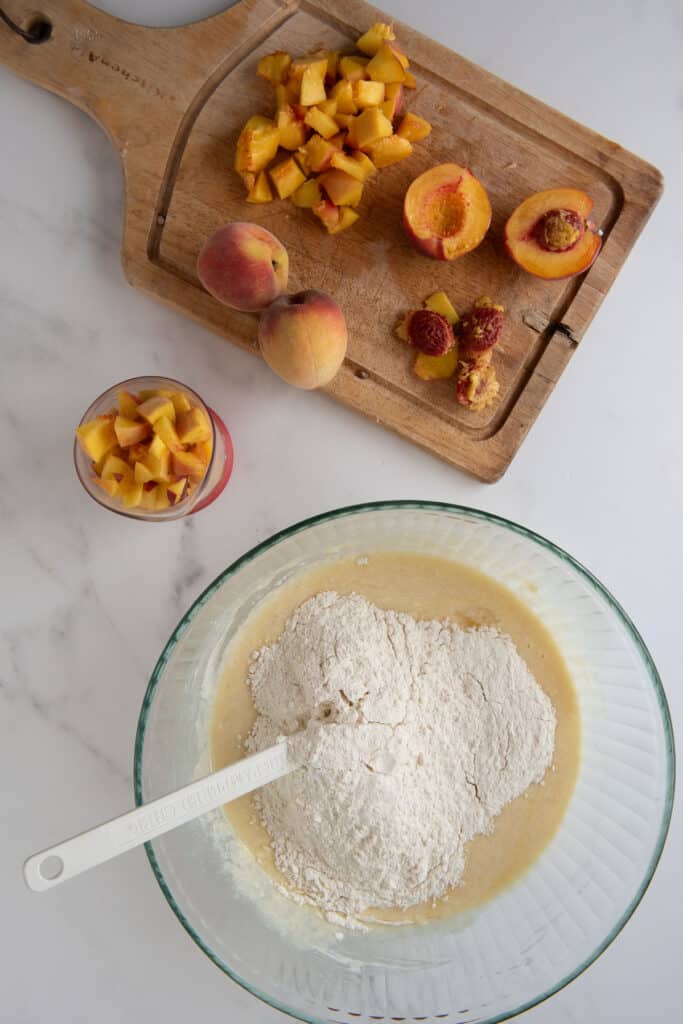 mixing bowl with ingredients for sourdough muffins next to cutting board with diced peaches