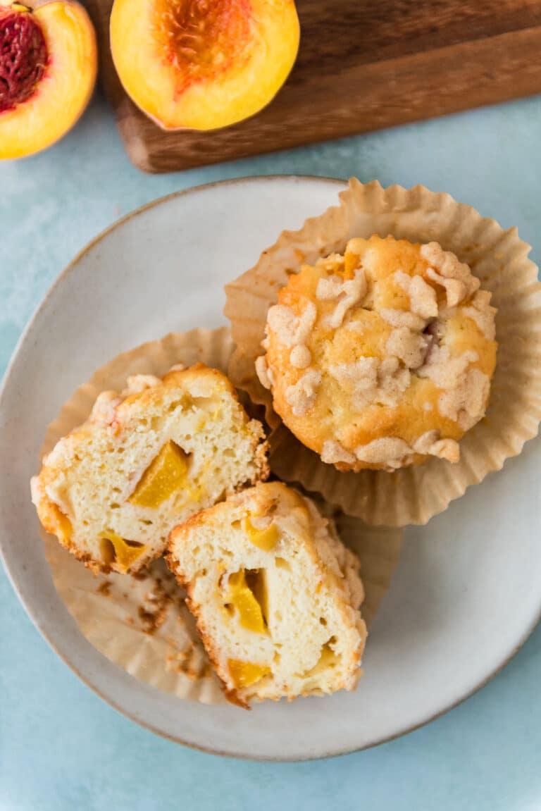overhead view of two sourdough peach muffins with crumble topping on grey plate, one cut open to show inside