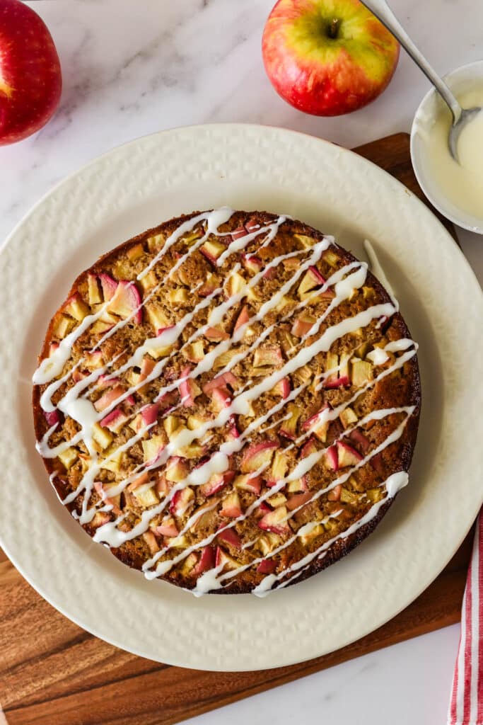 overhead view of sourdough apple cake with glaze on white platter with apples around plate