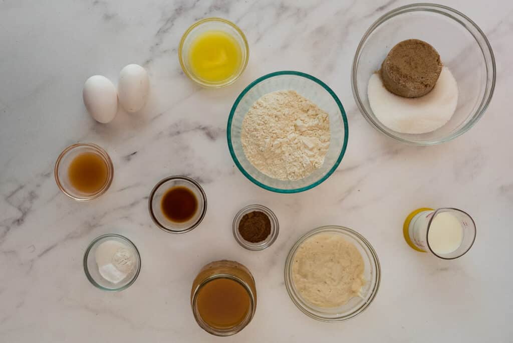overhead image of ingredients for sourdough discard apple cider donuts in glass bowls on marble counter