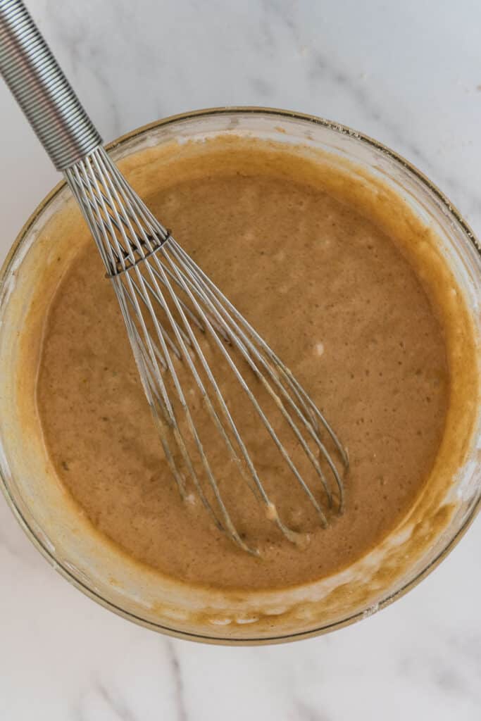 overhead view of large glass bowl with discard apple cider donut batter and whisk