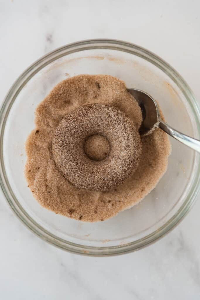 baked cider donut in bowl of cinnamon sugar