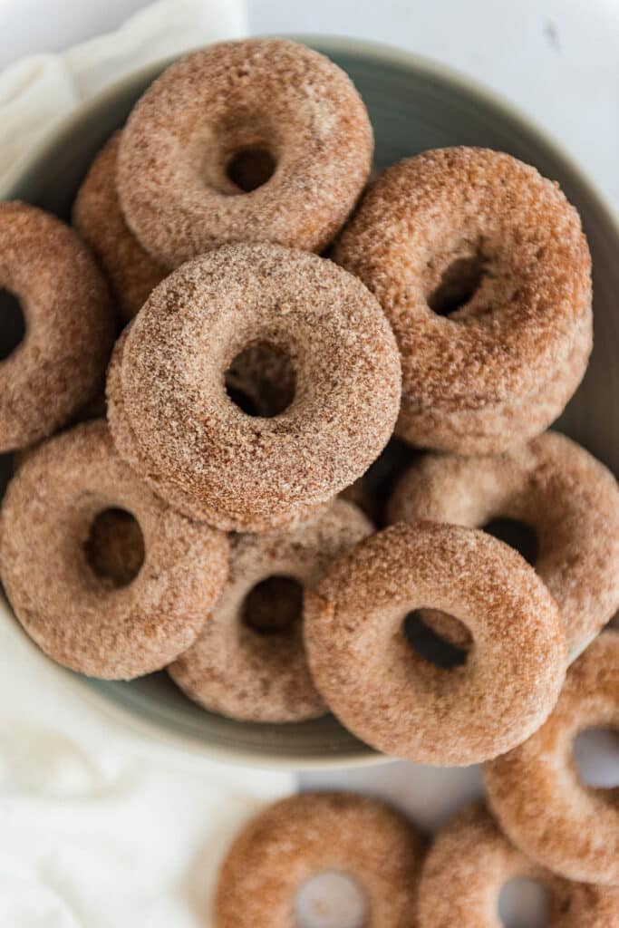 overhead view of grey bowl filled and overflowing with sourdough apple cider donuts coated in cinnamon sugar