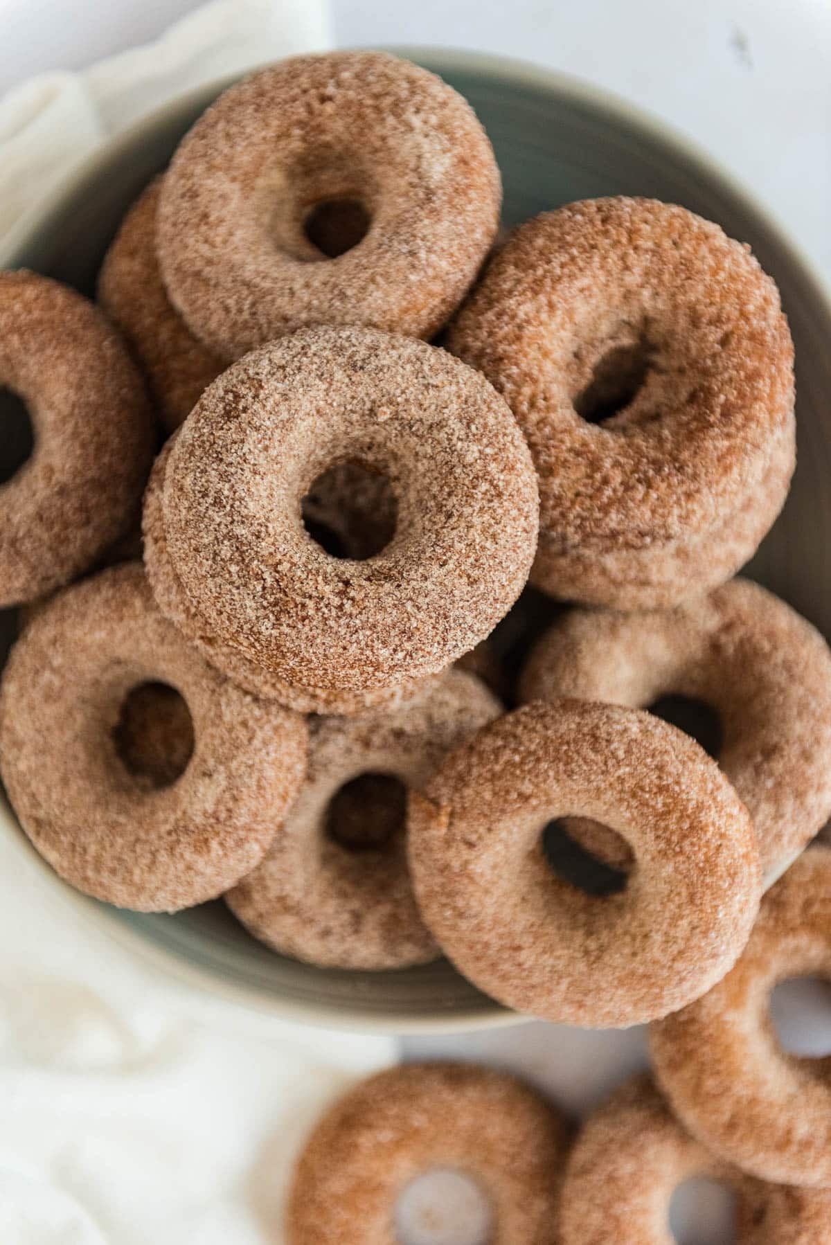 overhead view of grey bowl filled and overflowing with sourdough apple cider donuts coated in cinnamon sugar