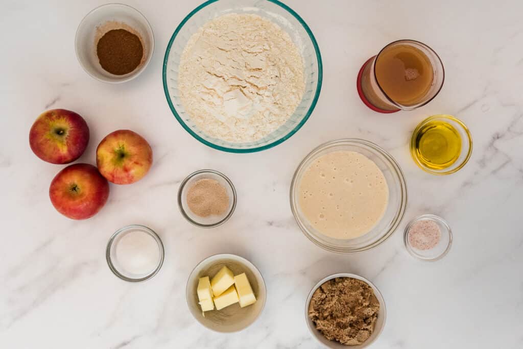 overhead of ingredients for sourdough apple cinnamon focaccia in glass bowls on marble counter