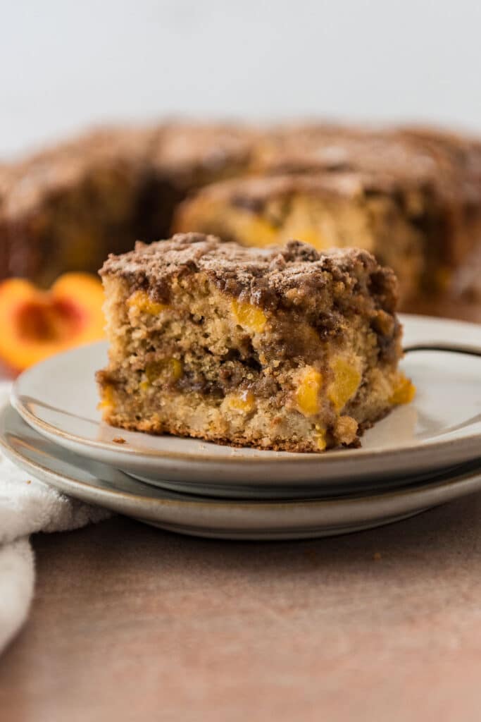 slice of peach sourdough coffee cake on grey plate with more cake in background