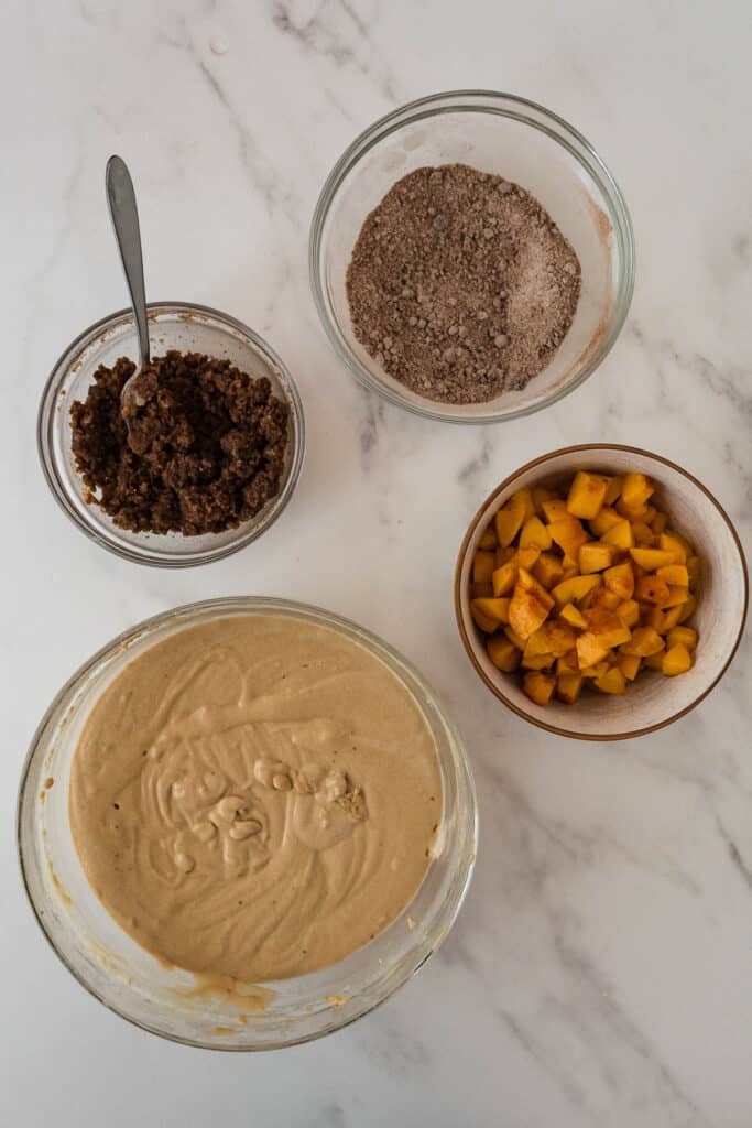 four bowls on marble counter, holding sourdough coffee cake batter, diced peaches, coffee cake filling and toppings