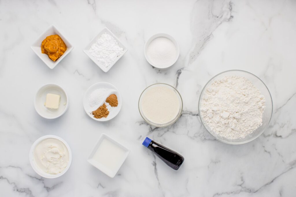 ingredients for sourdough pumpkin cinnamon rolls in glass bowls on marble counter