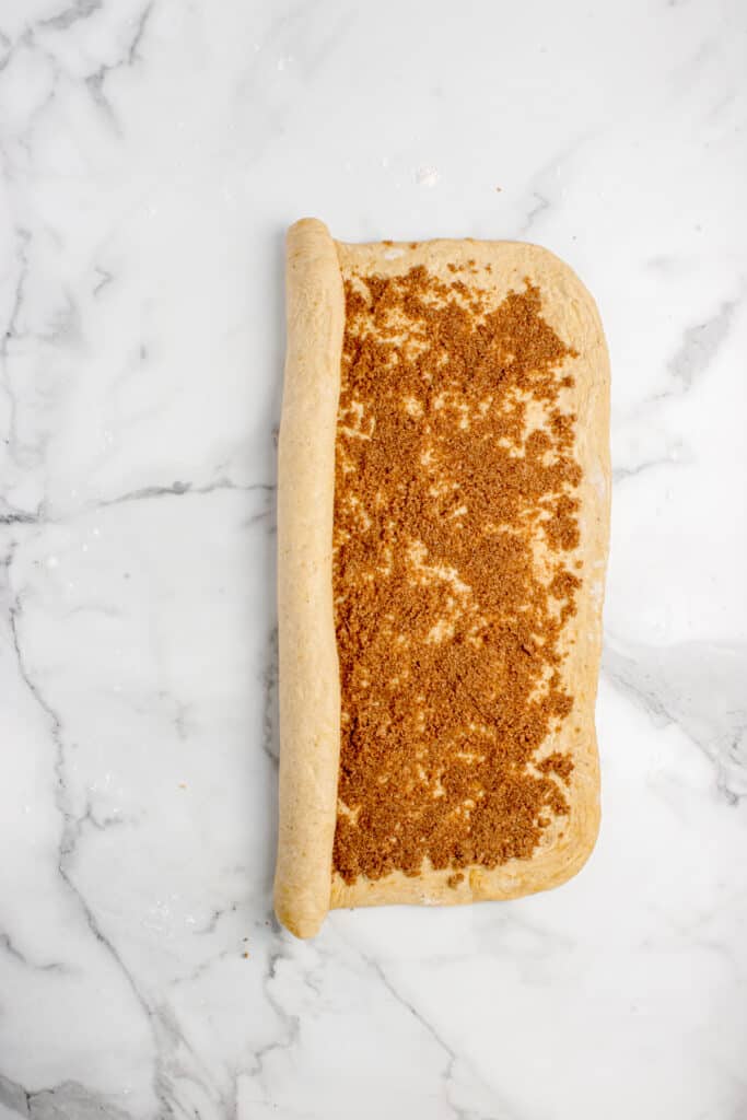 dough for cinnamon rolls rolled out and spread with filling and halfway rolled into log