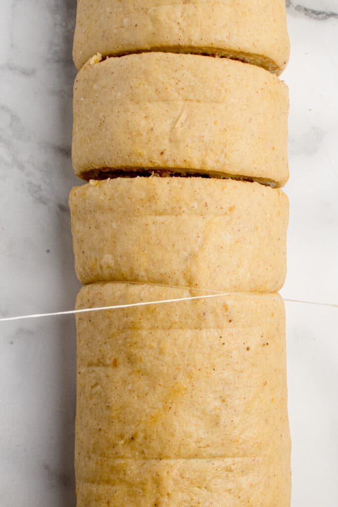 log of cinnamon rolls being cut into individual pieces by piece of floss