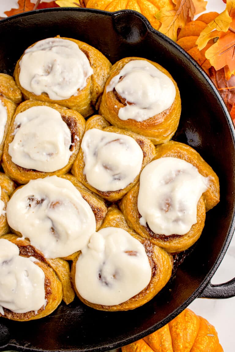 cast iron skillet with sourdough pumpkin rolls topped with cream cheese frosting