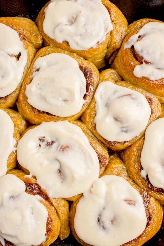 closeup image of sourdough pumpkin cinnamon rolls topped with cream cheese frosting