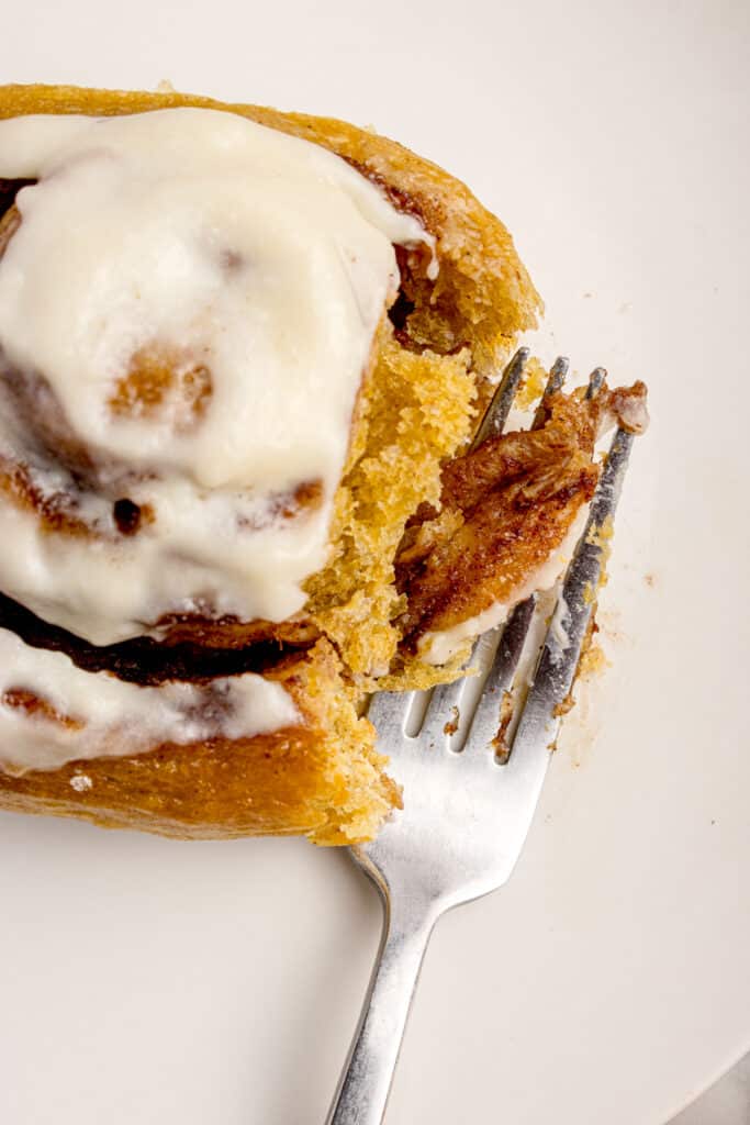 fork cutting into sourdough pumpkin cinnamon roll topped with cream cheese frosting