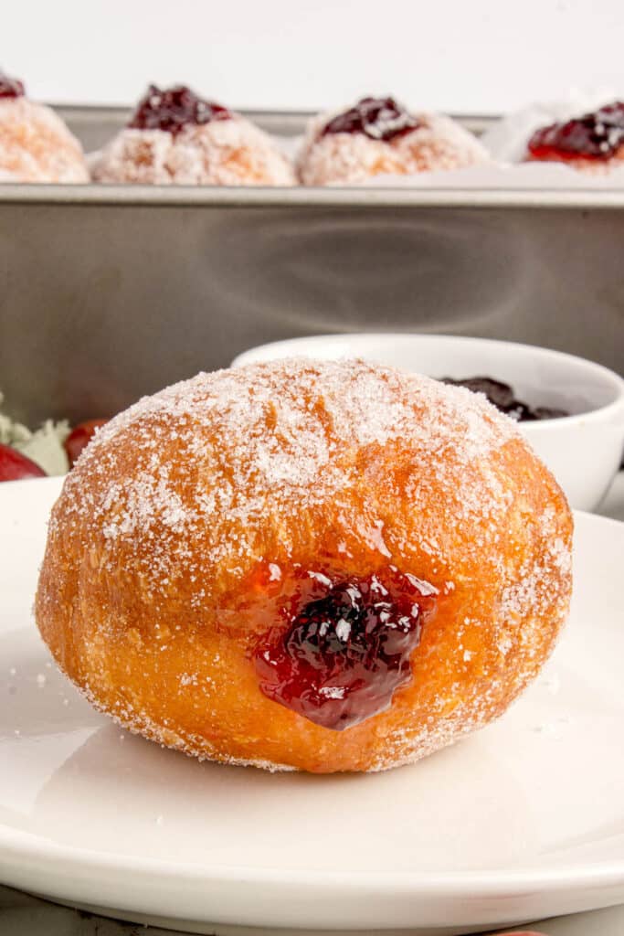 sourdough jelly filled donut on white plate with more donuts lined up in background
