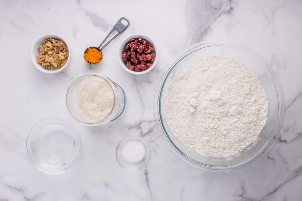 overhead image of ingredients for sourdough cranberry walnut bread in glass bowls 