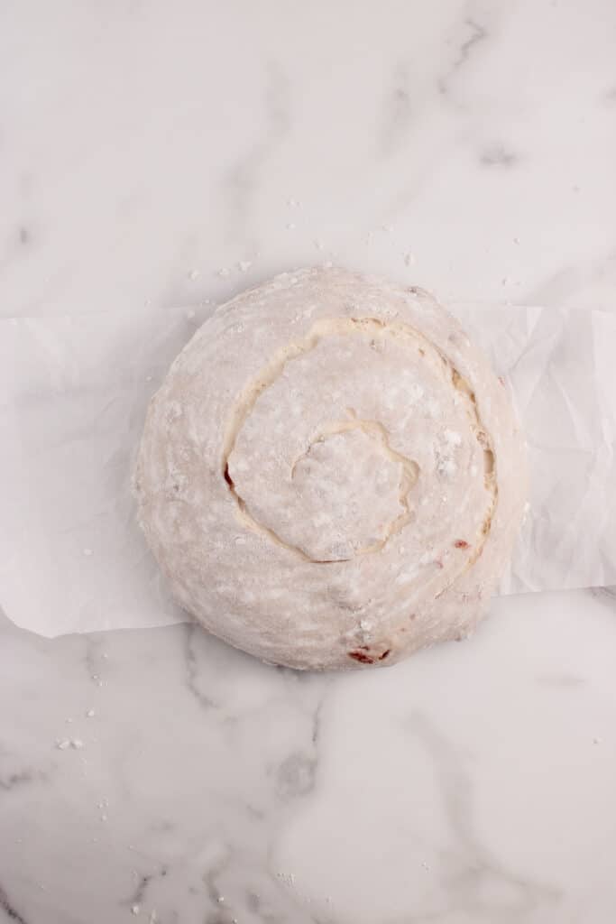 round loaf of dough on parchment paper with swirl score pattern