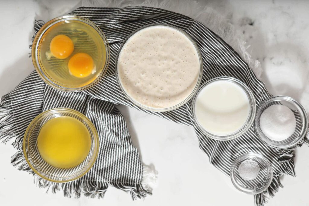 ingredients for sourdough crepes in glass bowls on marble counter