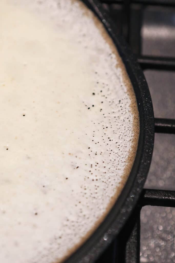 sourdough crepe batter cooking on skillet showing small bubbles